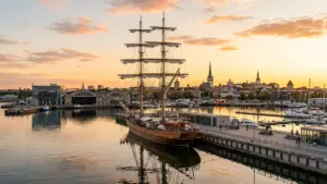 Suur purjelaev seisab Tallinna sadamas päikeseloojangul, taustal on Tallinna vanalinna siluett ja kirikutornid.