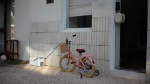 Roosa lapsejalgratas seisab moderne hoone ees, viidates noorte ja laste vaba aja tegevustele.