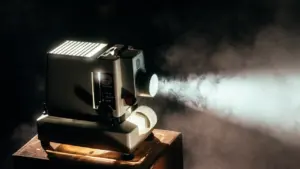 Klassikaline filmi-projektor pimedas ruumis, kiirgamas eredat valgusvihku suurele ekraanile.